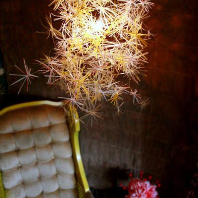 A spiky light above a white marshmellow backed chair with a yellow trim that sits next to a red and white flower.