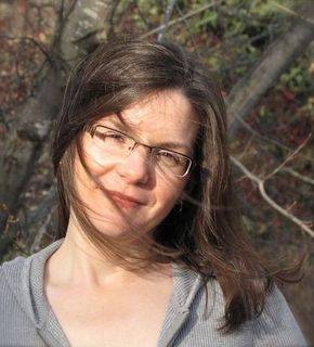 A middle-aged brunette woman with glasses posing in the middle of the woods.