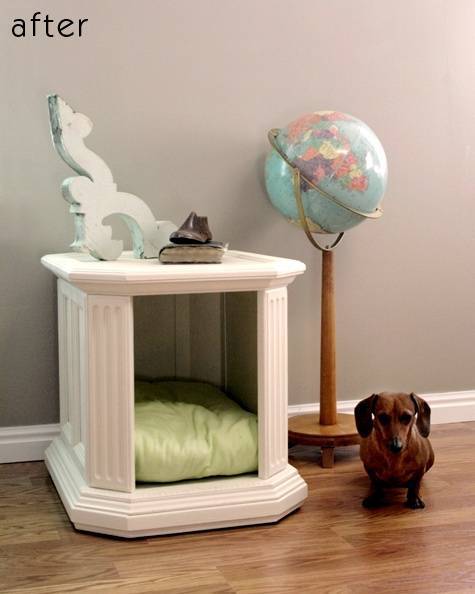 A white dog house with a light green cushion inside and a brown dachshund standing next to it and a globe on a stand behind him.