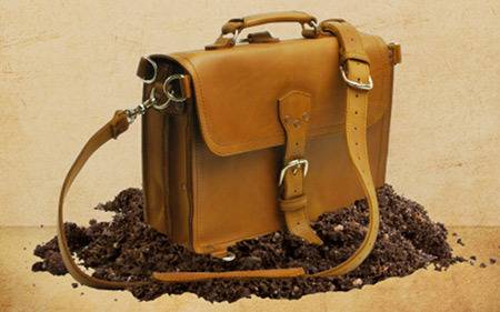 A briefcase made of thick leather sitting on a pile of dirt.