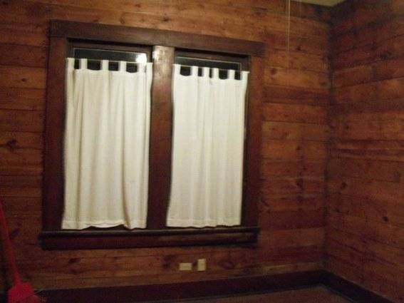 White curtains to a window in room with wooden walls.