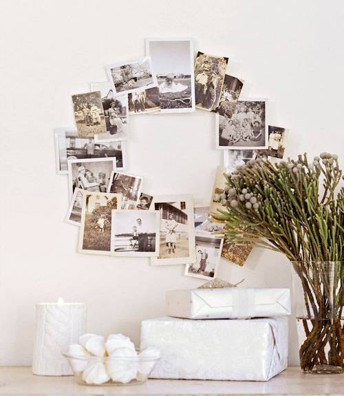 Photos are arranged in a circle on a wall over some greenery in a vase and two wrapped boxes.