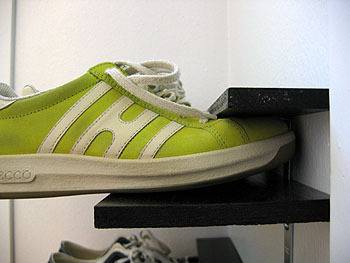 A green shoe hanging off a shoe rack.