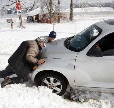 Two men trying to push a PT Cruiser out of the snow from the front.