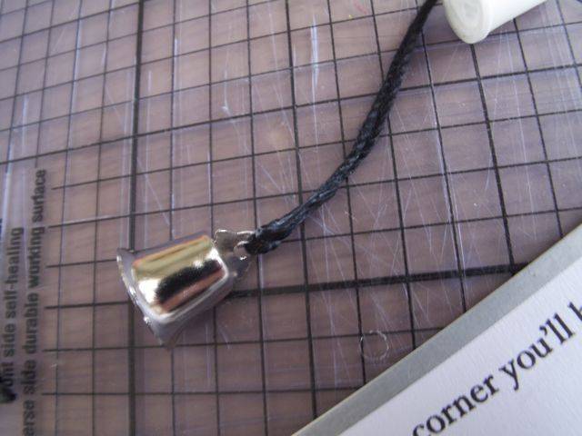 A silver bell is attached to a braided black cord.