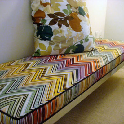 Rainbow colored chevrons decorate the fabric on a bench with a colorful floral pillow on top.