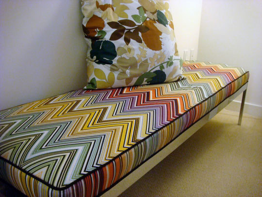 Rainbow colored chevrons decorate the fabric on a bench with a colorful floral pillow on top.