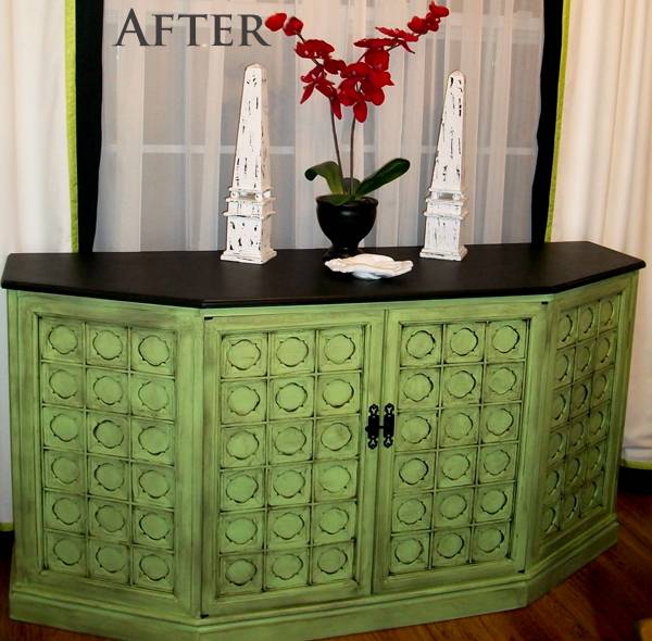 A four door green and black cabinet lying near window with a vase on top of it.