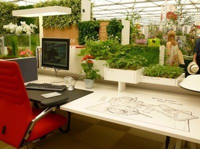 A greenhouse workstation with plants scattered all over the computer desk.