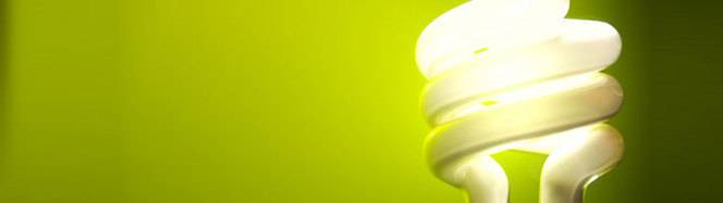 A lit energy saving bulb with a bright green wall backdrop.