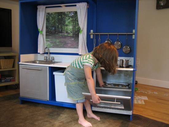 A young girl putting a cookie tray in a small oven in a blue kitchen.
