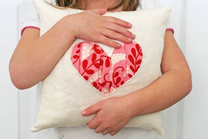 A young girl holding onto a pillow with a heart design in the middle of the pillow.