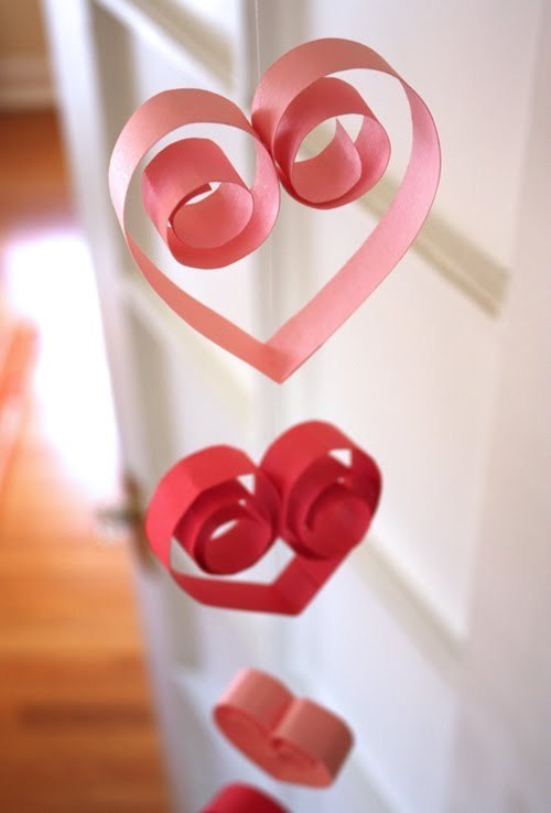 Pink and red quill papers folded in heart shape hanged to a tread in an order.