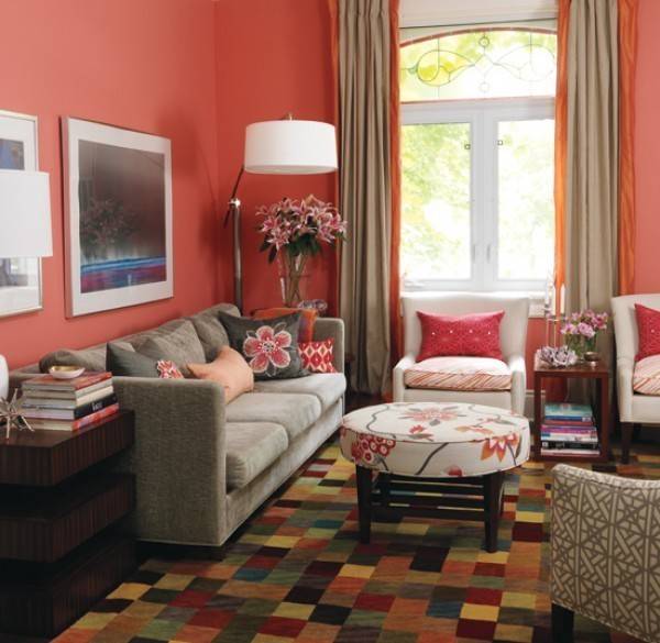 Living room with red shaded walls and cushion, table, chairs, lamp, flower vase and wall frames inside.