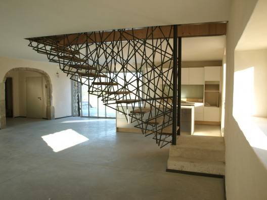 A large living room having staircase in the middle which is made of metal pipes.