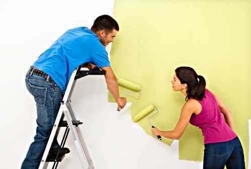 Man and woman holding paint rollers and painting a white wall green.