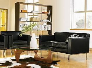 Living room comprising black sofa set and black glass table with a white vase on top of it.