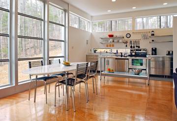 A very large, bright kitchen and dining room in one with glossy wooden floors and giant floor to ceiling windows.