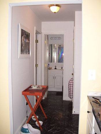 A hallway leading to the bathroom with an ironing board in the center.