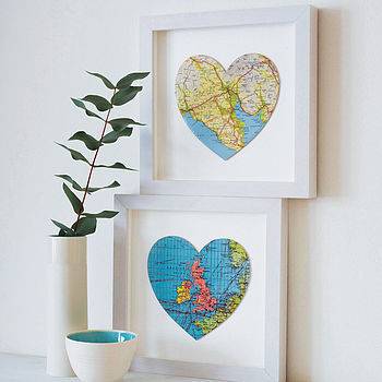 Two framed pictures of heart-shaped maps with a bowl and a tall thin flower pot sitting in front and to their left