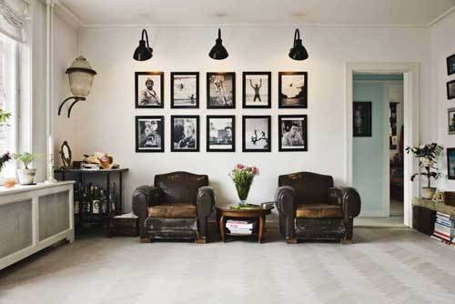 A living room with two leather sofas, with lights over hanging them illuminating pictures.