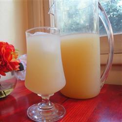 A pitcher and a drinking glass intended for alcohol contain a murky peach colored beverage.