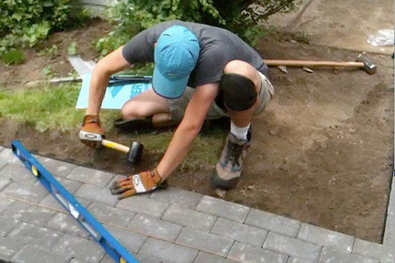 A man installing stone tiles in a yard.
