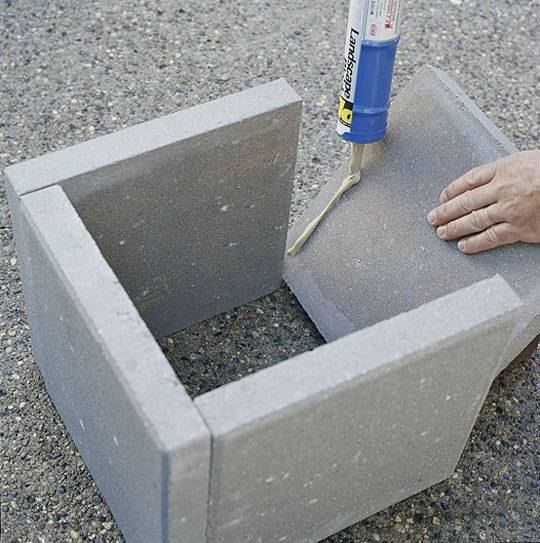 A person setting up four cement blocks together outside.
