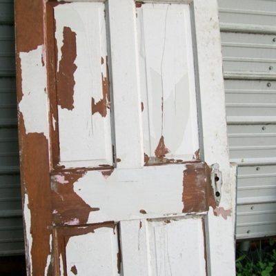 An old, worn down door with a lot of its white paint scraped off.