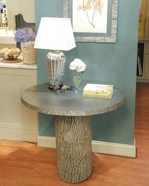 Round table with tree stump base table light and flower vase on top.