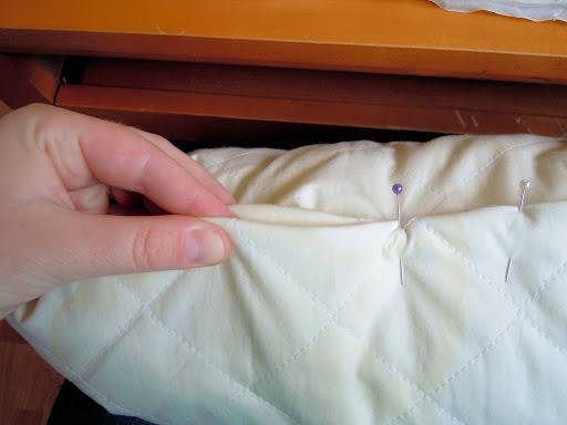 A hand holding a quilt with some sewing needles in it.