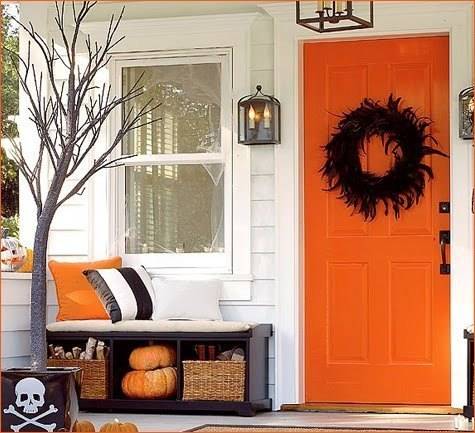 Orange color front door with lamps on both sides and rack cushion aside.