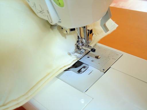 White bed pillow case being sewn together using a white sewing machine.