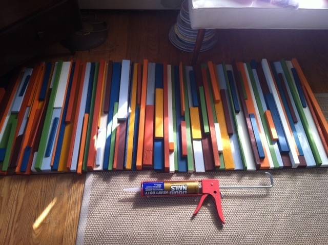 A glue gun and many sticks painted in various different colors stacked above.