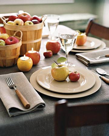 A table setting with apples on the plates and a couple of baskets of apples on the table.