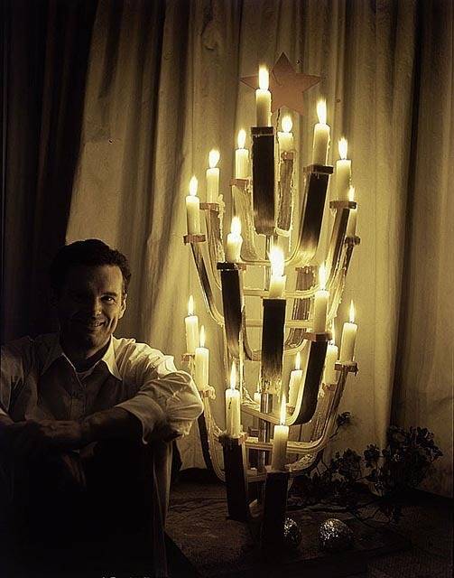 A statue of lit candles in the dark next to a man.