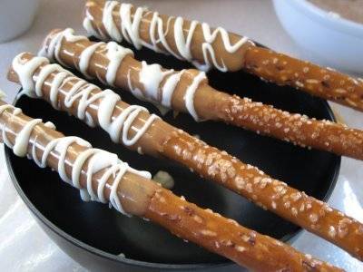 Four pretzel sticks have icing on them and are sitting over a black plate.