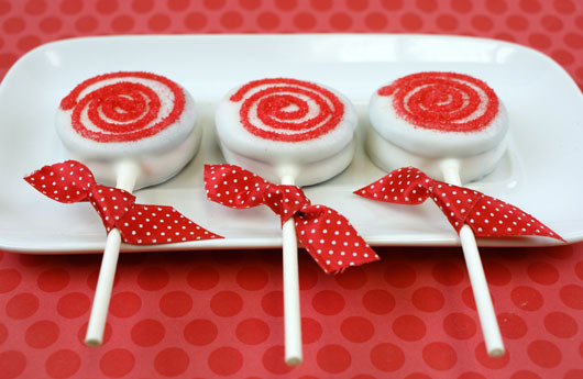 Red and white desserts are sitting together on sticks with red bows.