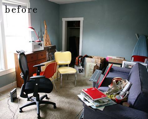 A black chair and a white chair in a blue room with a blue sofa with junk on it.