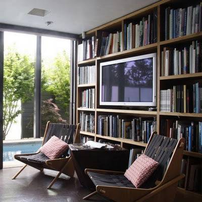 A TV in the middle of a wall full of books and two chairs beneath it.
