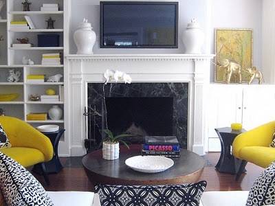 A television sitting above a fireplace in a white room with black and yellow decorations.