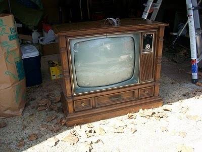 An old console television is sitting near the door of a garage.