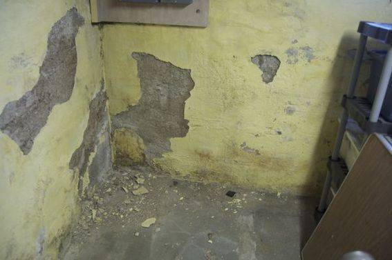 A badly deteriorated basement with green paint chipping all over the place.