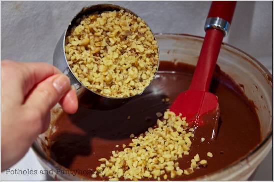 A person is mixing nuts into a chocolate confection.