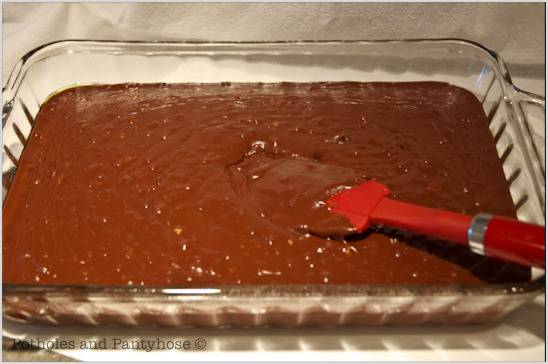 A clear glass rectangular baking dish contains raw brownie or chocolate cake batter.
