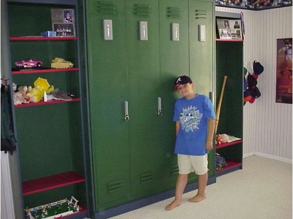 A young boy in a dark baseball cap leaning against a row of tall green lockers.