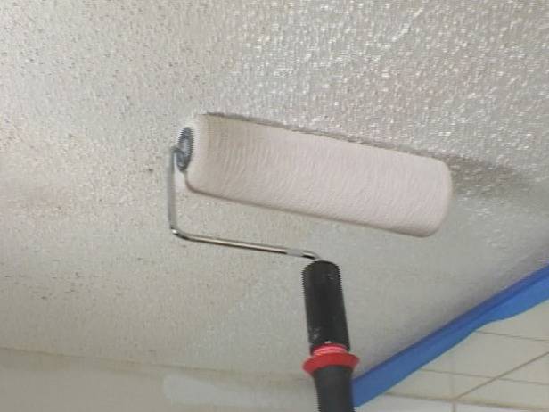 A black extension is holding a paint roller as it paints over a popcorn ceiling.