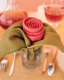 " A decorated red rose flower made by napkins  place in a dining table"