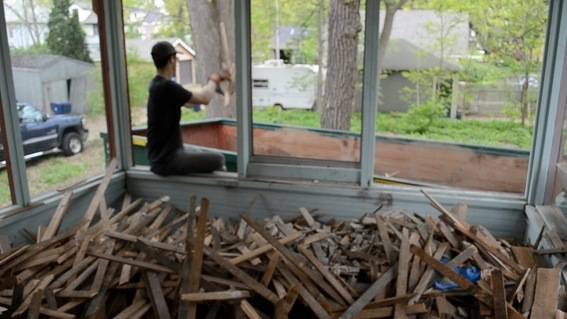 A man works at the window of a room filled with used planks.