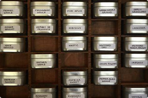 A spice cabinet displays many squat silver jars of spices.